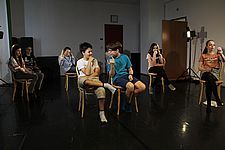 Foto von sieben Schüler/innen, die auf Sesseln sitzend eine Szene im Klassenzimmer spielen